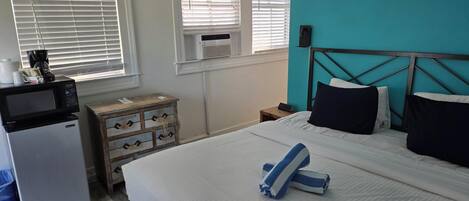 Un dormitorio con cama, mesita de noche, cómoda, microondas y ventana con persianas.