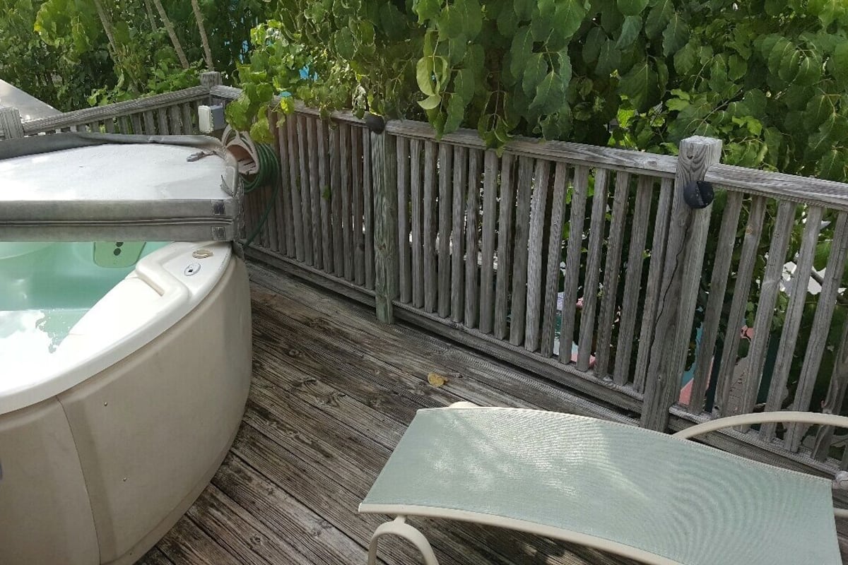 A hot tub on a wooden deck with a metal chair and a wooden fence in the background.