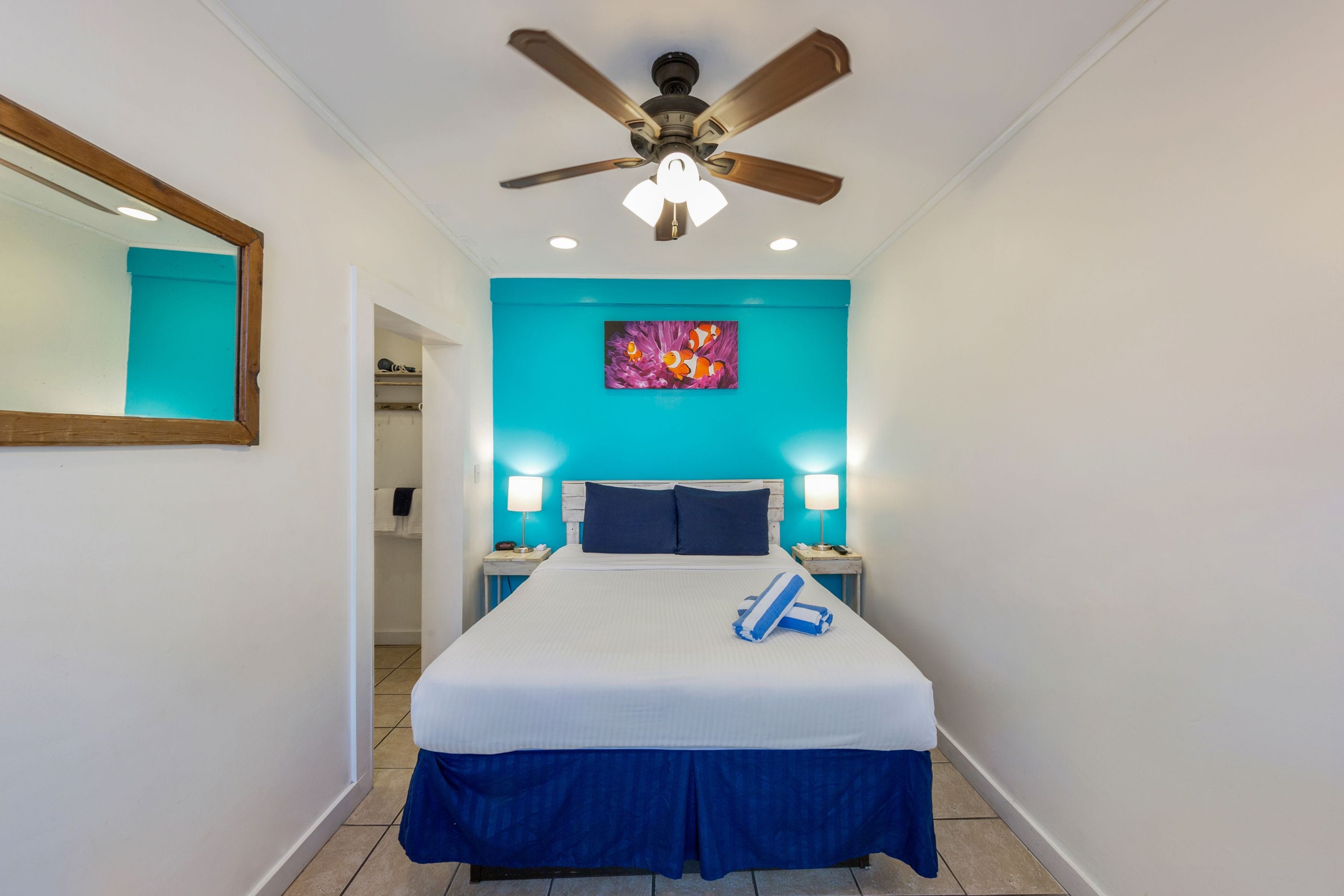 A hotel room with a bed, a ceiling fan, a painting, and two bedside lamps.