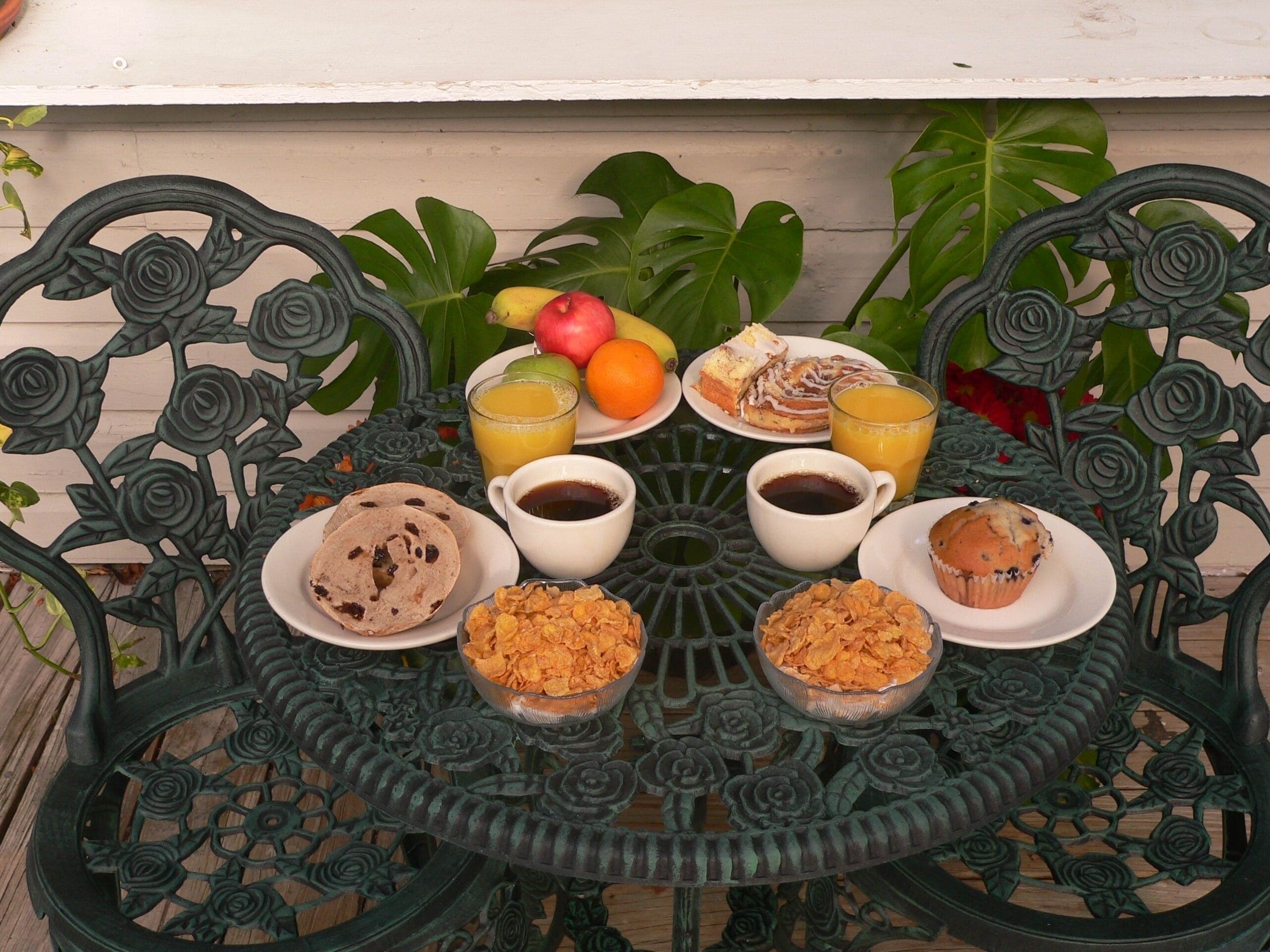 A round table with a floral metal design, surrounded by various breakfast items including pastries, fruits, and beverages.