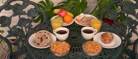 A round table with a floral metal design, surrounded by various breakfast items including pastries, fruits, and beverages.