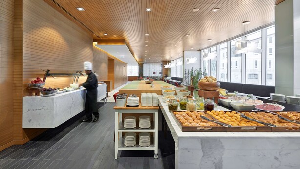 A modern buffet setup with a chef preparing food, a variety of dishes, and a seating area with tables and chairs.