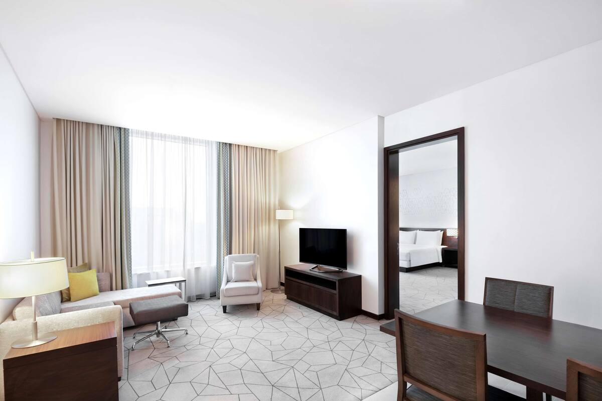 Een hotelkamer met een bank, fauteuil, televisie, eettafel en een grote spiegel.