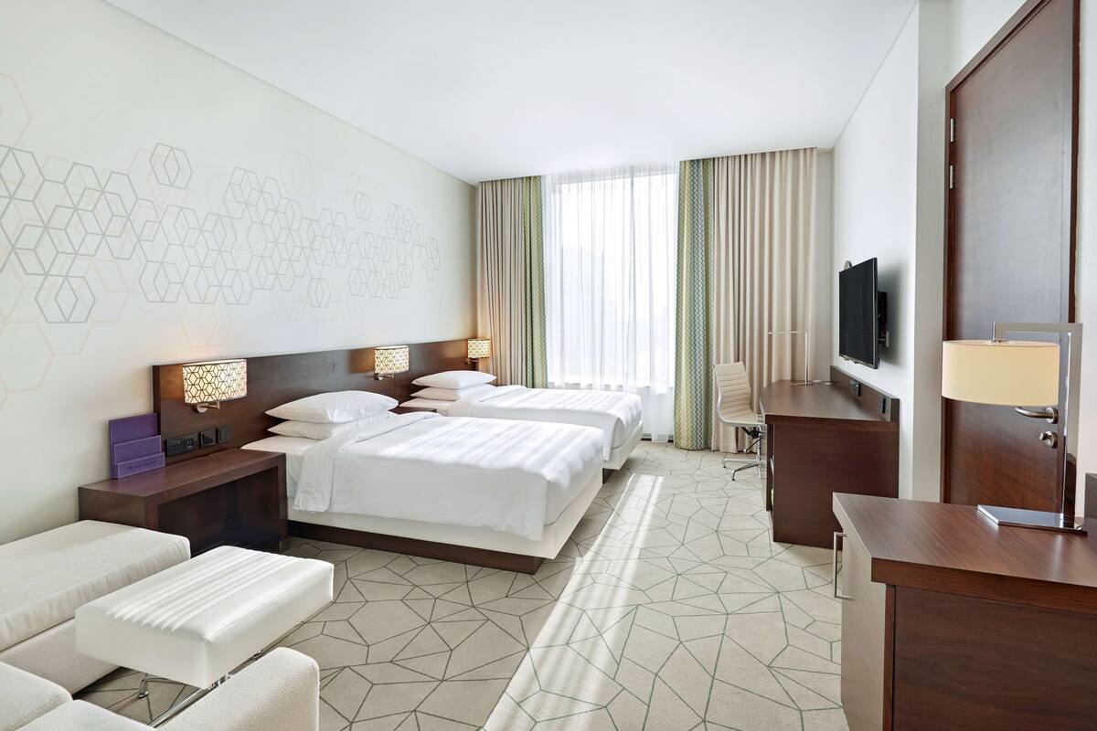 Een hotelkamer met twee bedden, een bureau met een televisie, een bank en een kamer met een patroon.