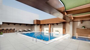 A modern indoor pool area with a clear pool, lounge chairs, and a bar area.