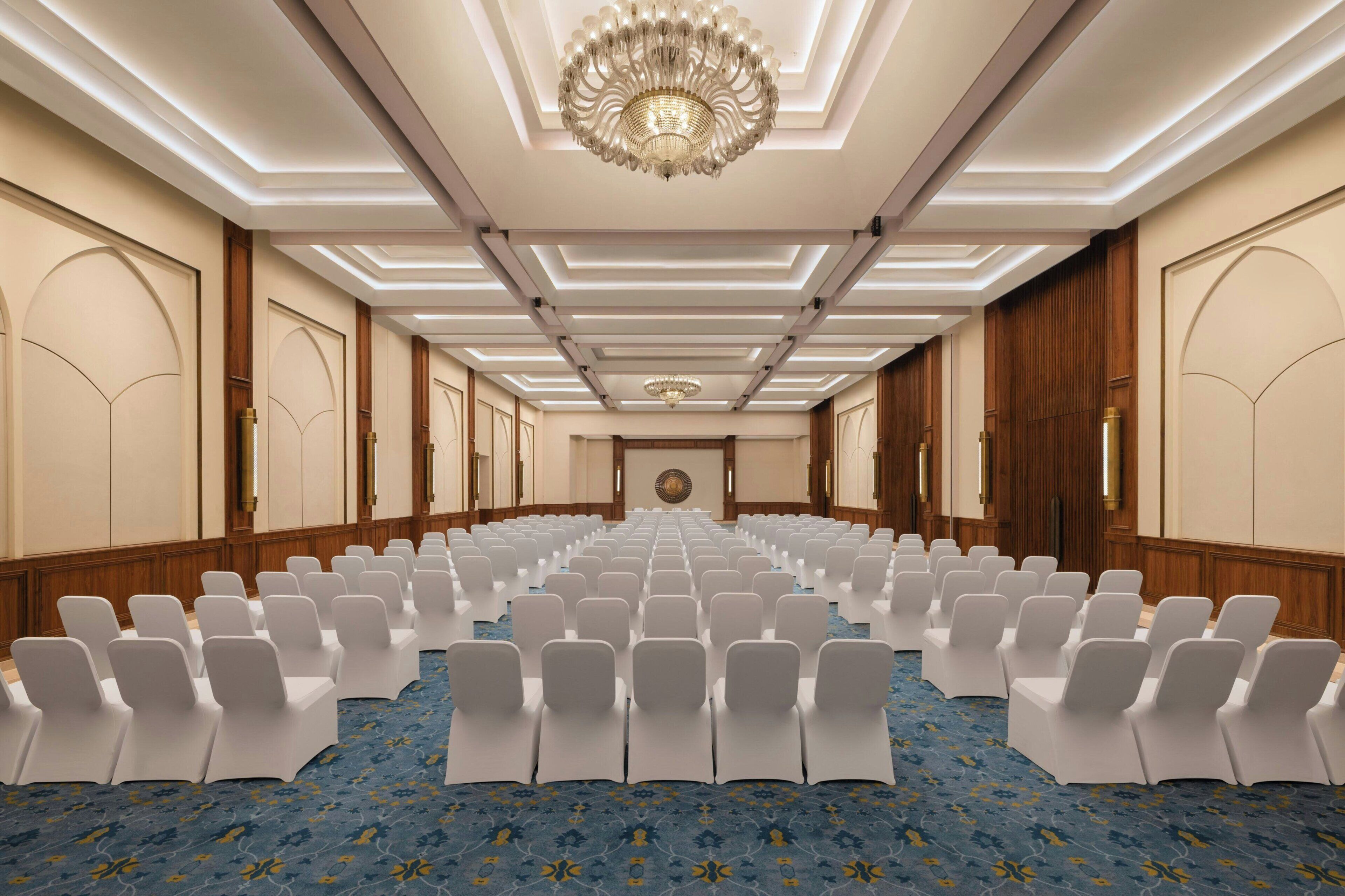 A conference room with rows of white chairs, a patterned carpet, and a chandelier.