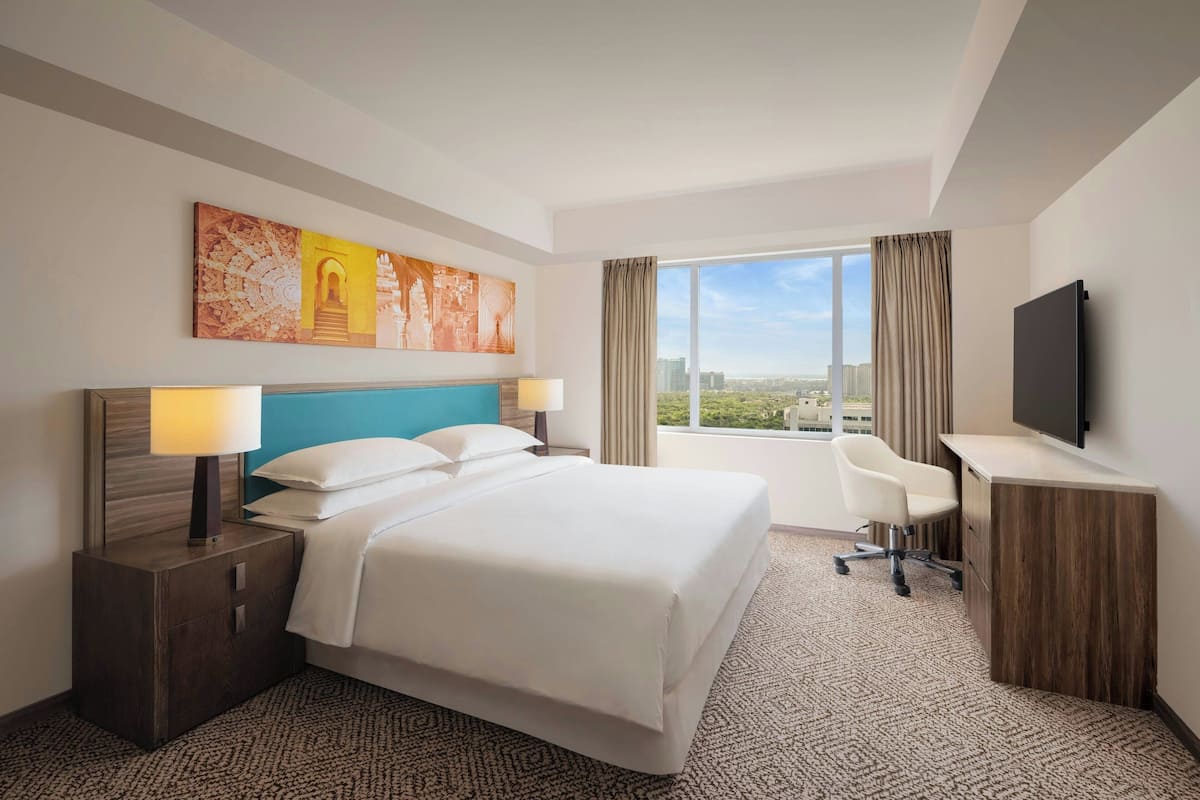 Ein Hotelzimmer mit einem großen Bett, einem Schreibtisch, einem Fernseher und einem Fenster mit Blick auf die Stadt.