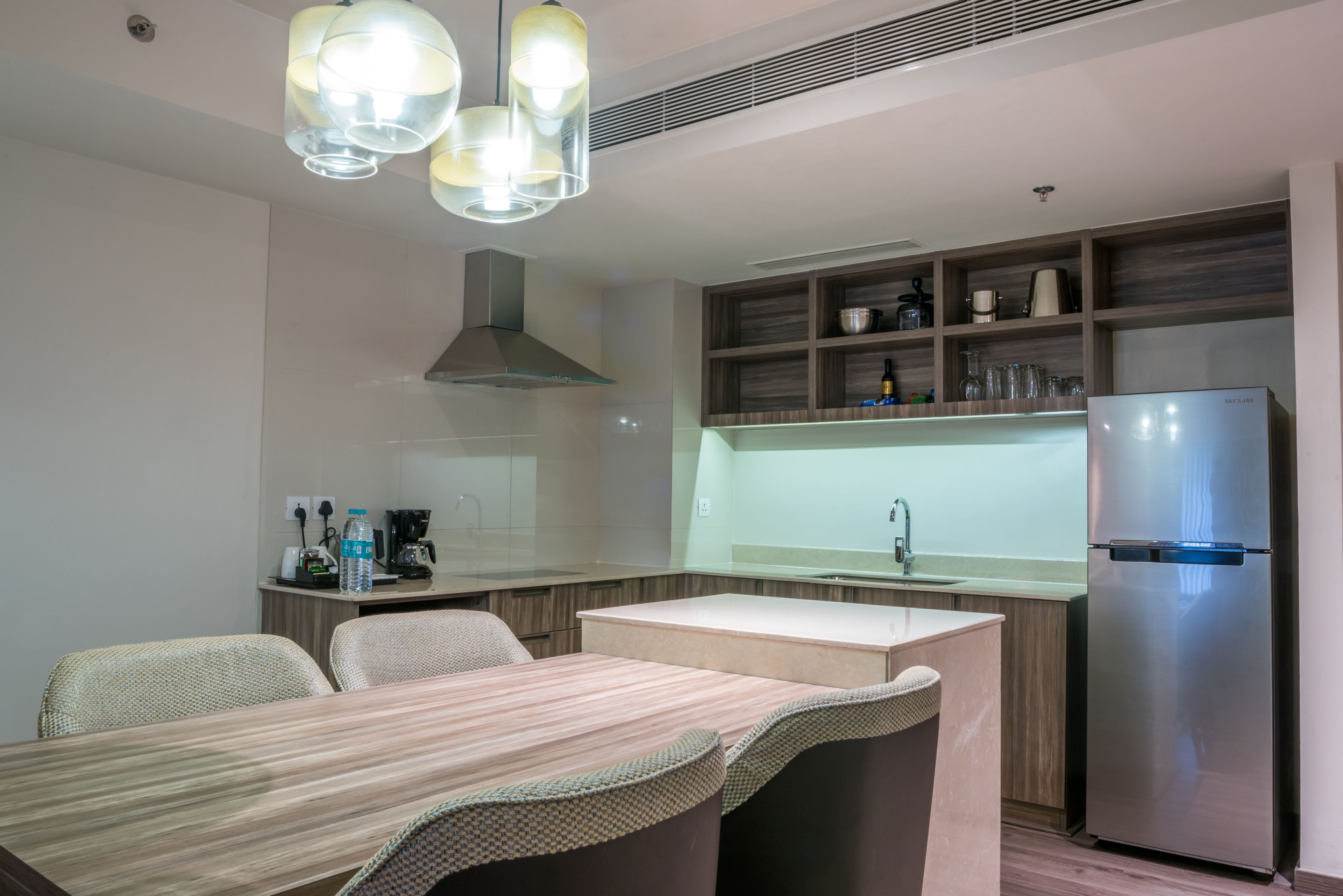 Una cocina moderna con isla integrada, refrigerador de acero inoxidable e iluminación colgante.