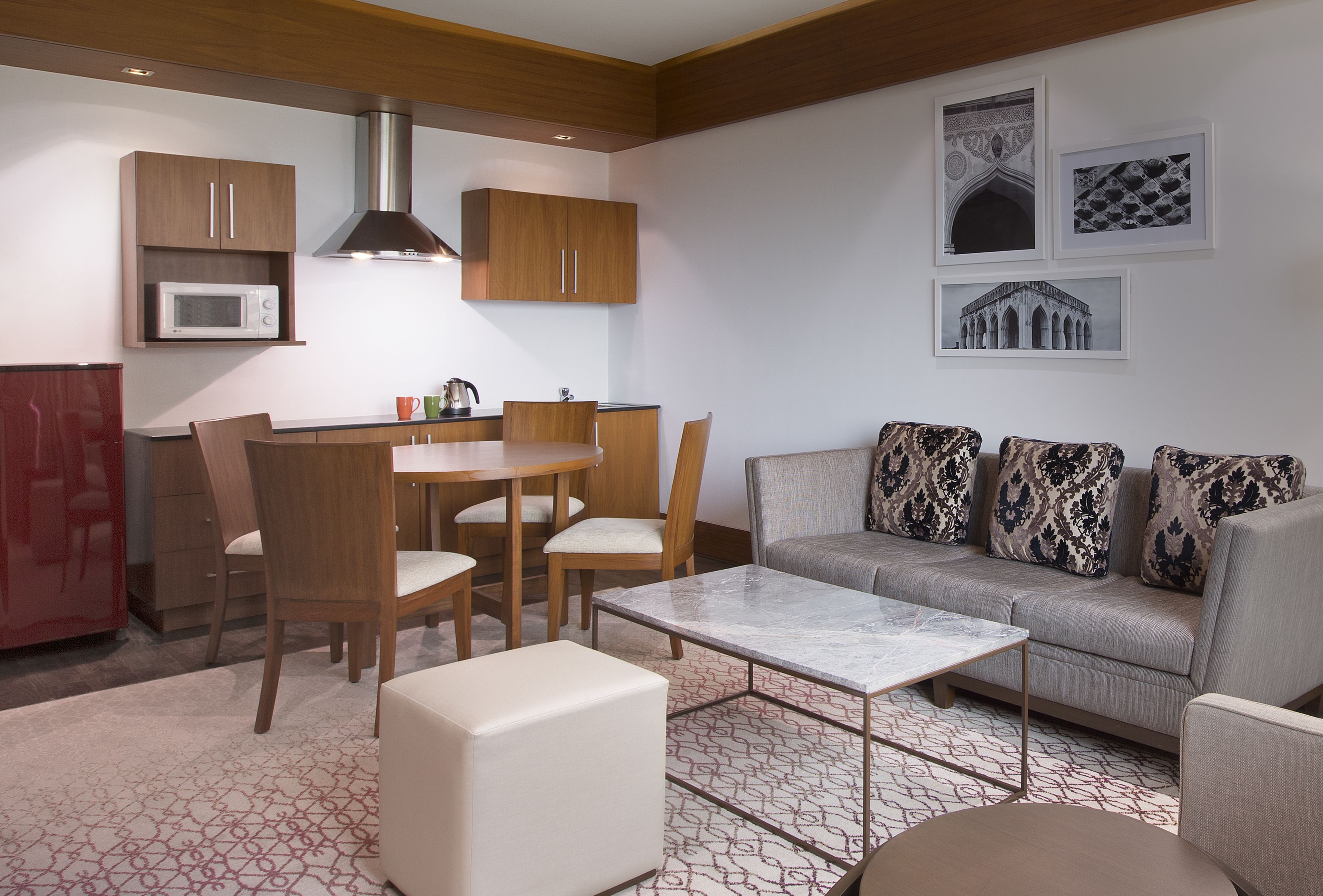 A modern living room with a sofa, chairs, a coffee table, and a dining area with a table and chairs. There is a microwave above the cabinets and artwork on the wall.