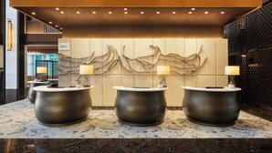Een receptiezone met drie zwarte receptiebalies, een grote muur met een golfachtig ontwerp en een plafond met inbouwverlichting.
