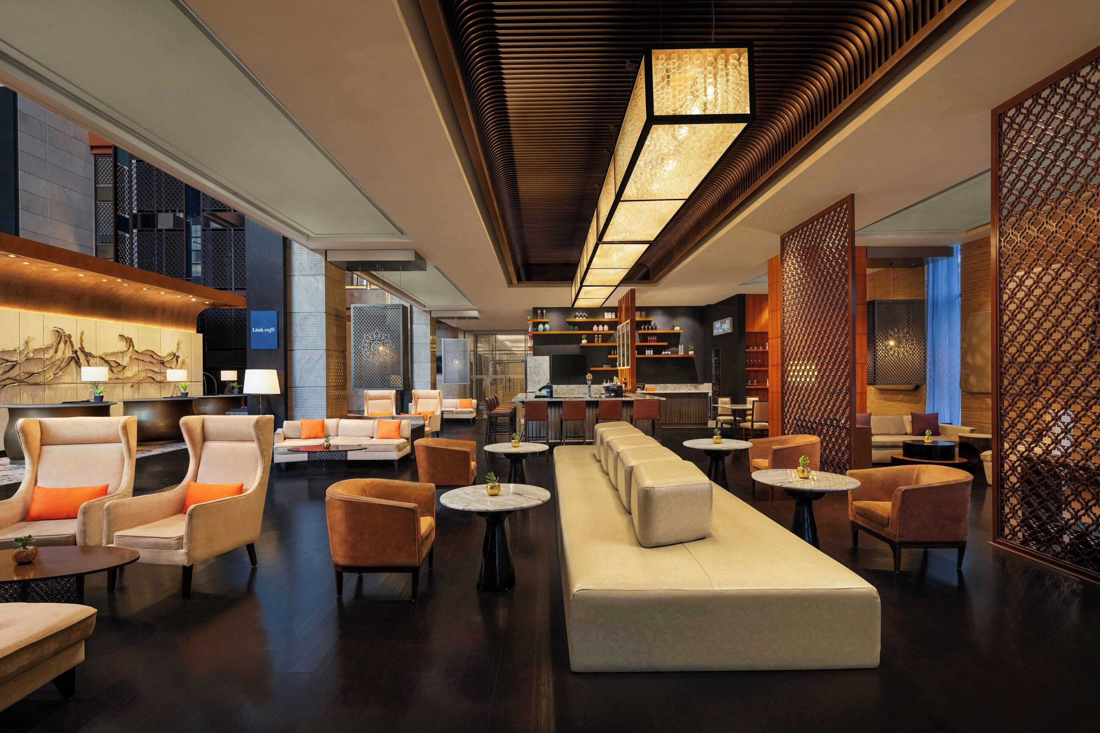 A modern hotel lobby with seating areas, a reception desk, and a bar.