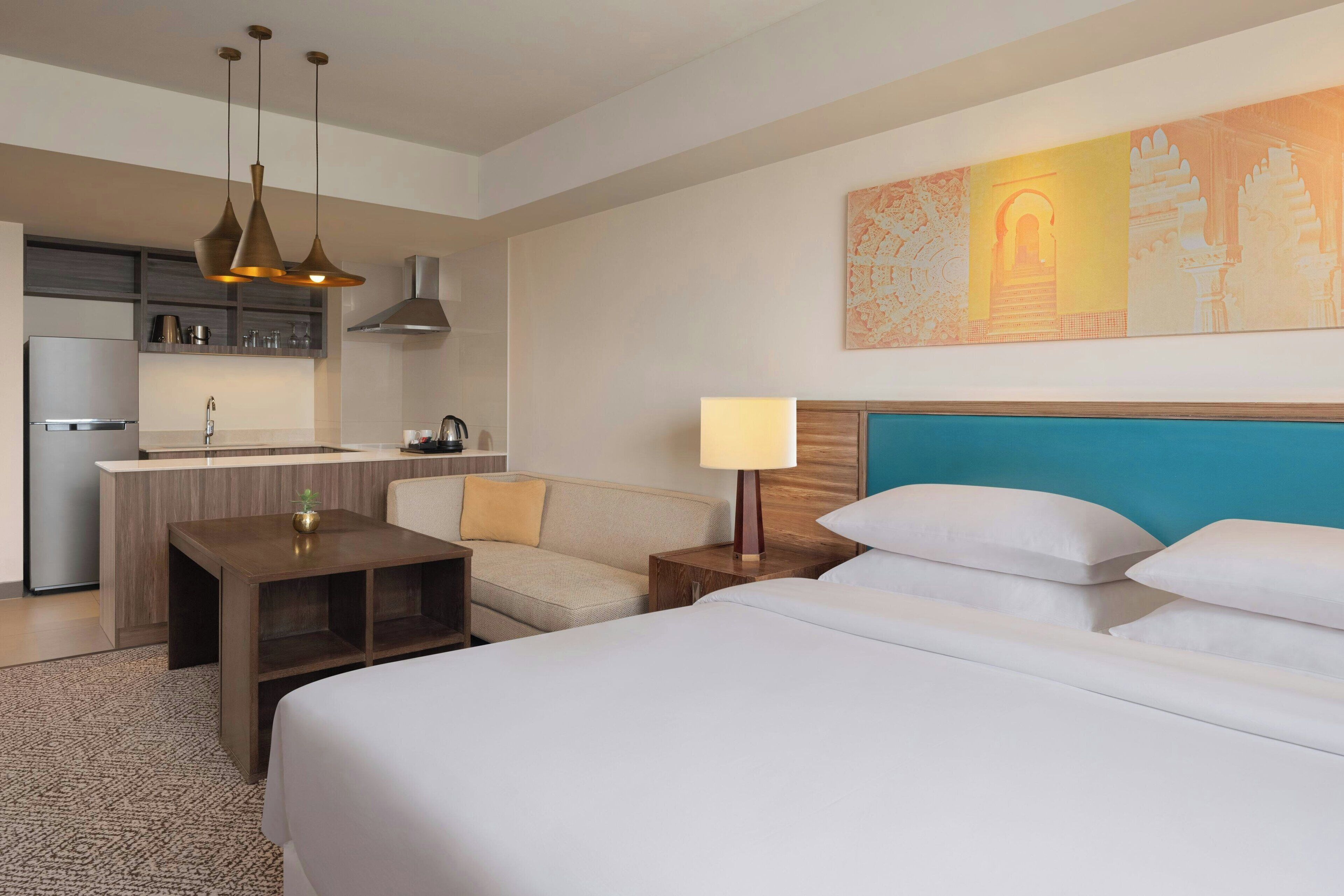 A hotel room with a bed, bedside table, lamp, and a painting on the wall.