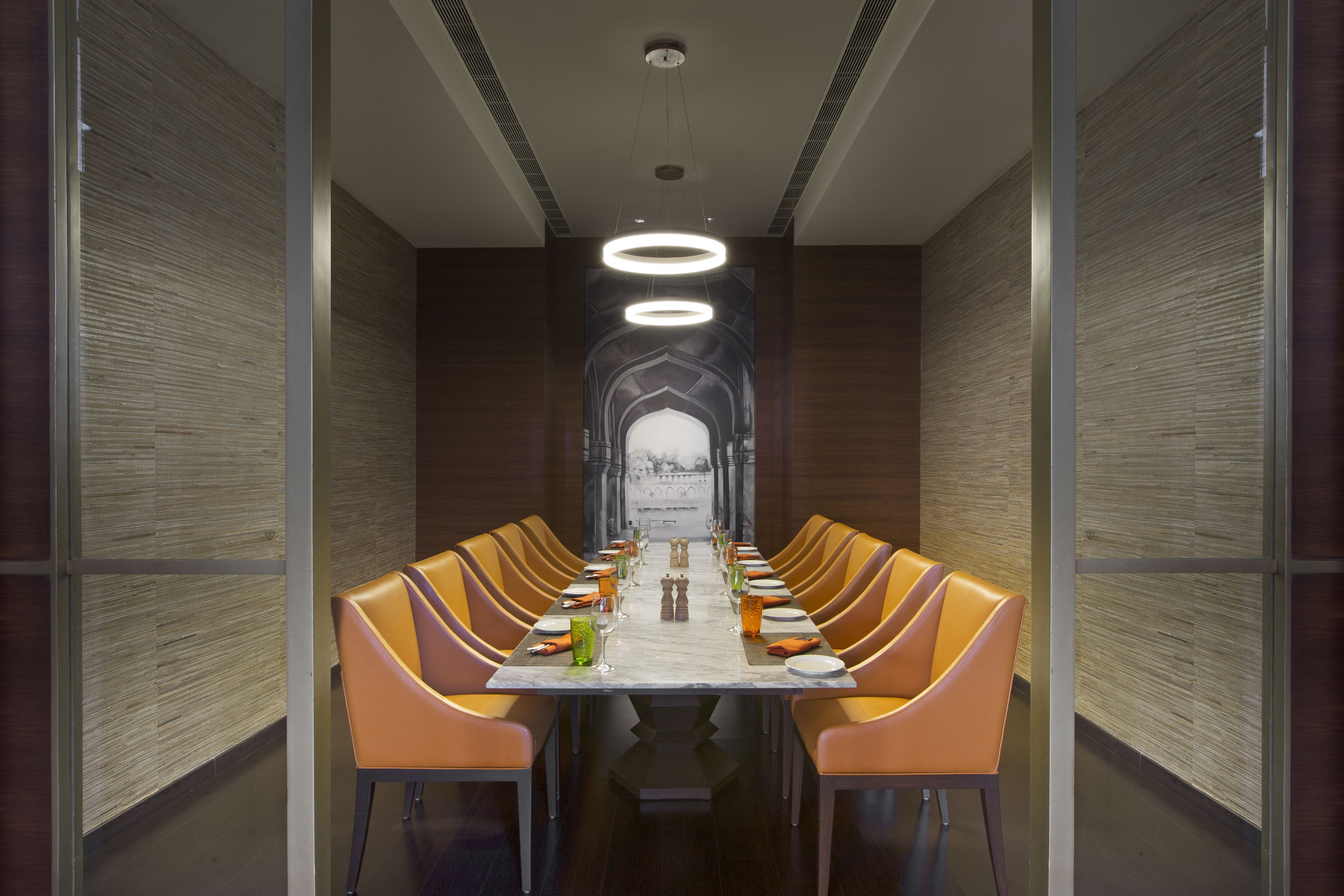 A long dining table with orange chairs, a marble top, and a modern chandelier.