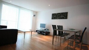 A modern living room with a flat-screen TV, a glass dining table with four chairs, and a large abstract painting on the wall. - Dreamhouse Apartments London (London)