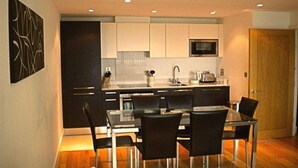 A modern kitchen with black and white cabinetry, a microwave, and a dining area with a glass table and black chairs. - Dreamhouse Apartments London (London)