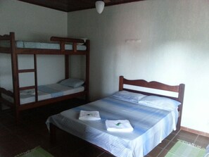 A room with bunk beds and a single bed, both with white linens.