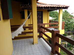 A yellow building with a wooden balcony, a hammock, and tiled flooring. - Itaúna Hostel (Saquarema)