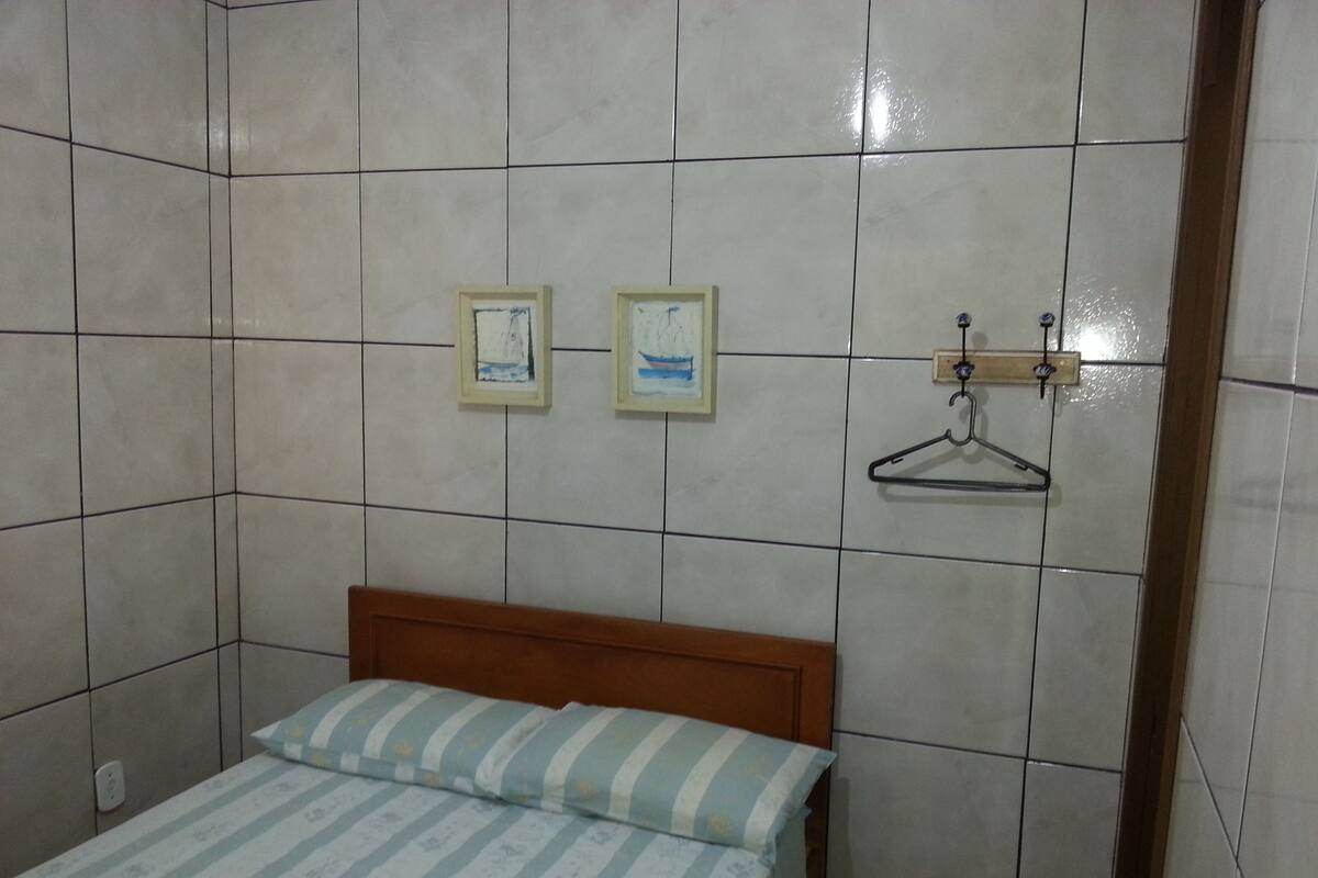 A small, tiled room with a bed, two framed pictures, and a coat hanger.
