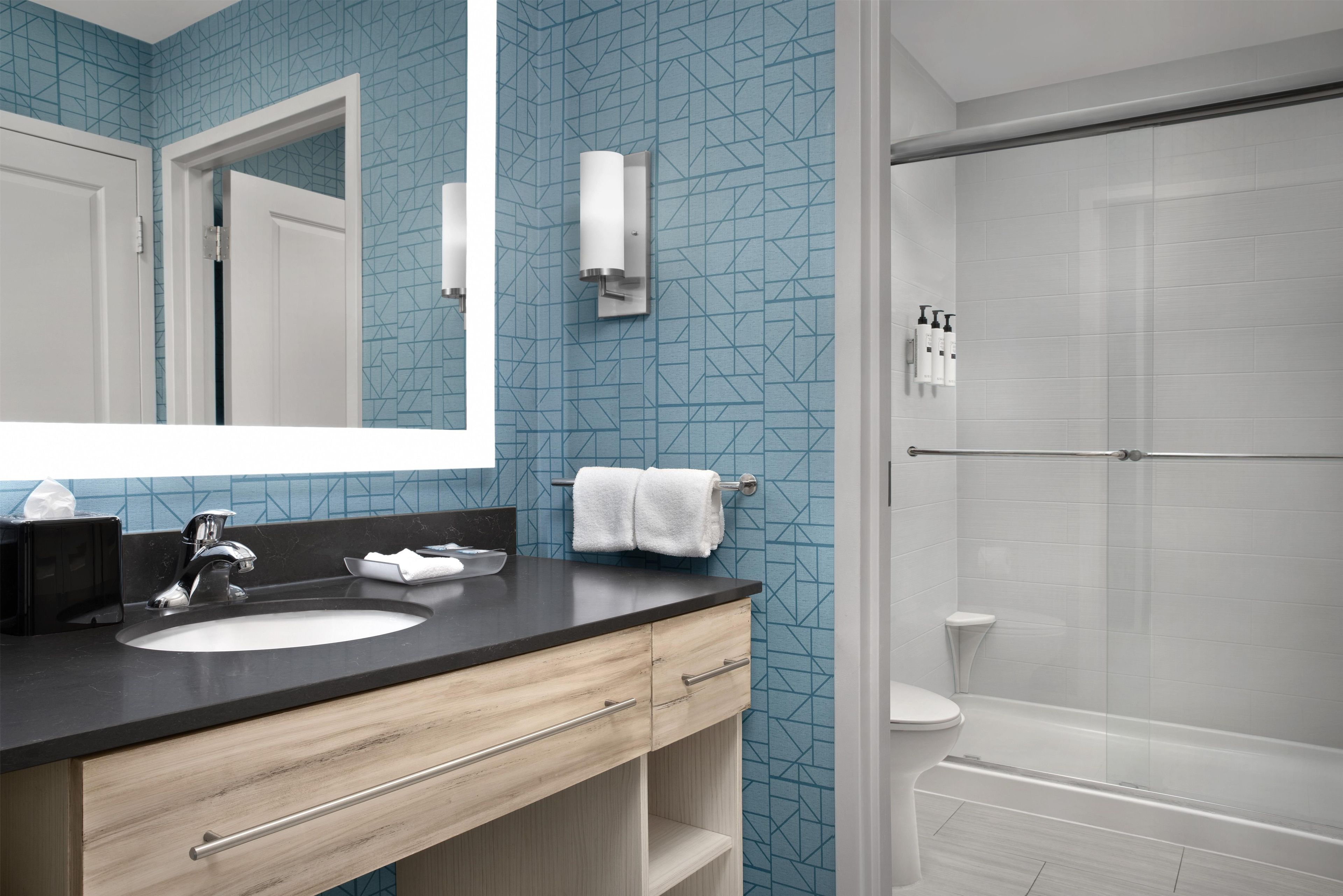 A bathroom with a sink, mirror, towel rack, and a shower area.