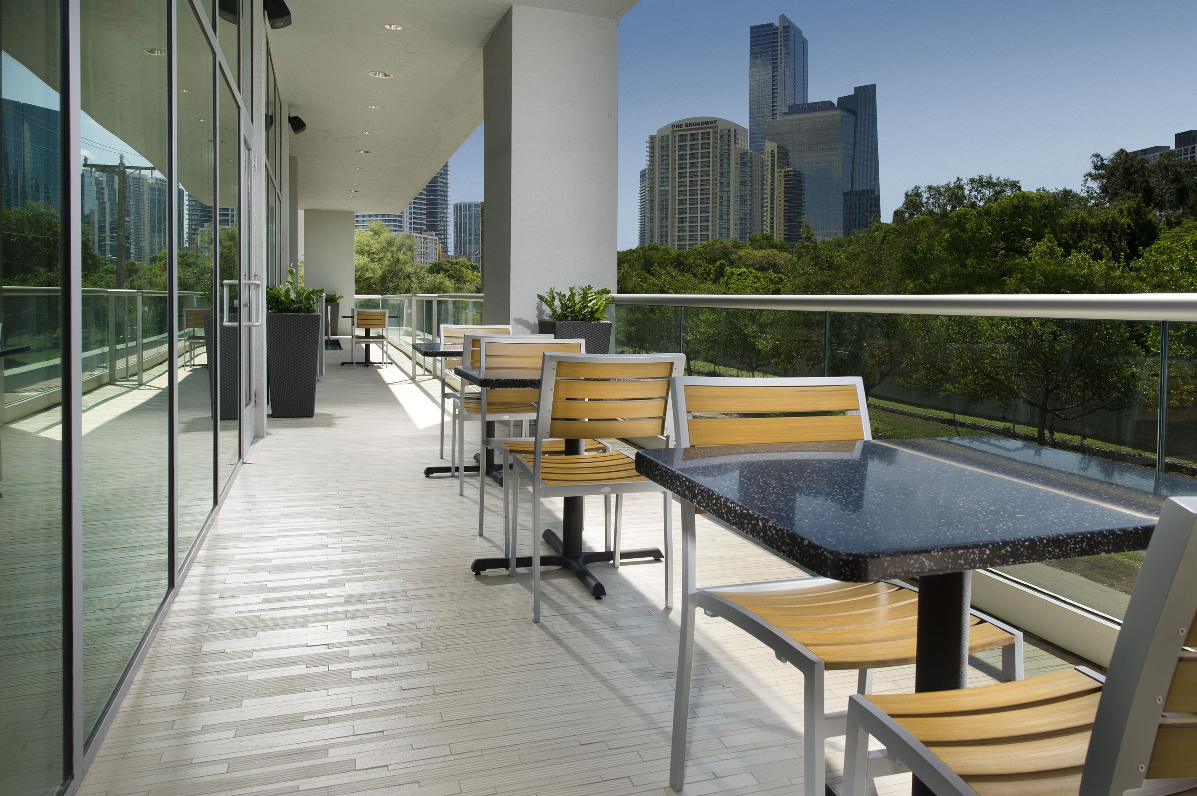 A balcony with a table and chairs, overlooking a cityscape with tall buildings.