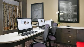 Een receptiebalie in een hotel met twee computerschermen, een klok en ingekaderde kunstwerken.