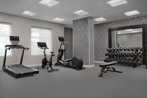 Un gimnasio con cintas de correr, bicicletas estáticas, una máquina de remo y una prensa de pesas.