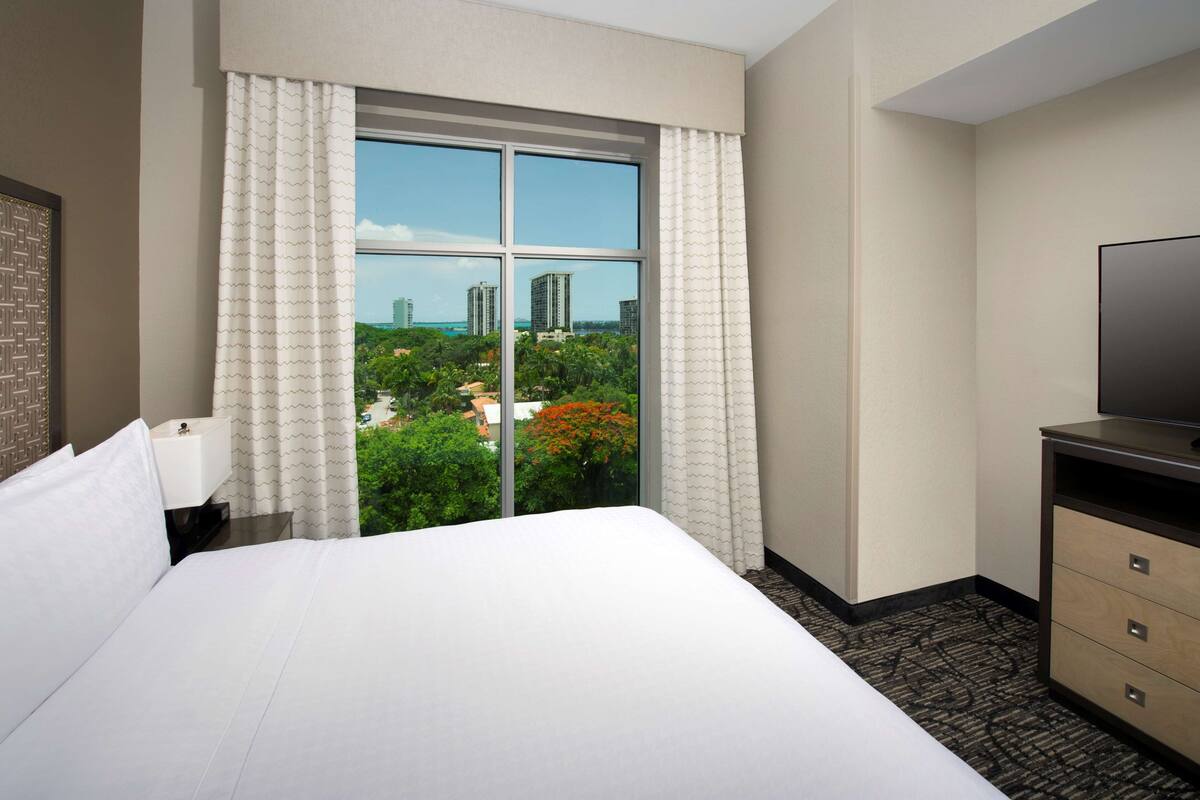Een hotelkamer met een groot bed, een televisie, een dressoir en een raam met gordijnen.