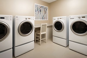 Une buanderie équipée de quatre machines à laver blanches, d’une chaise et d’une œuvre d’art accrochée au mur.