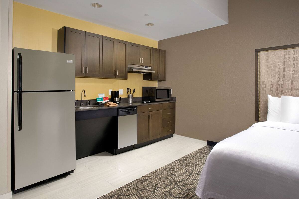 Een compacte hotelkamer met kitchenette, inclusief een koelkast, magnetron en gootsteen.