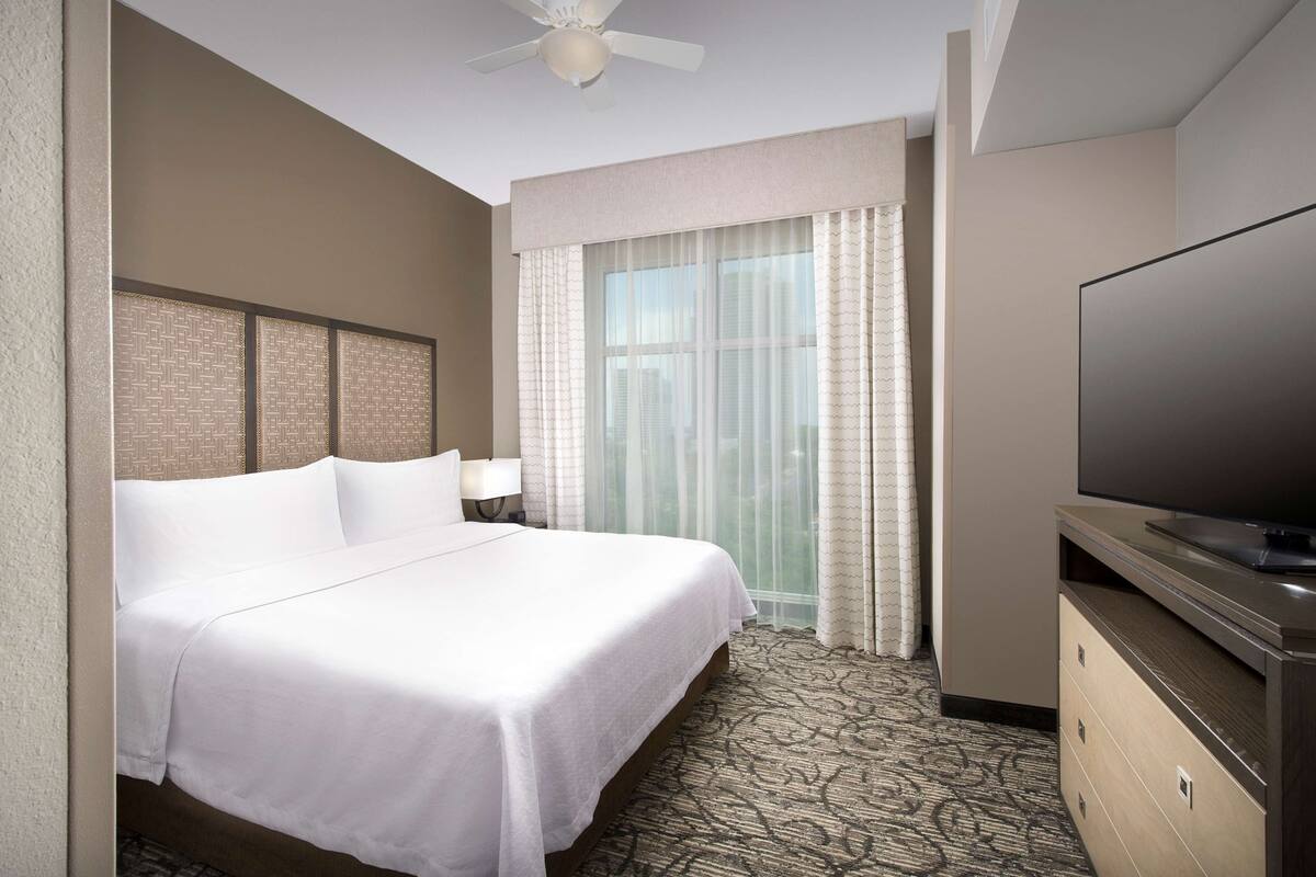 Een hotelkamer met een bed, een televisie, een plafondventilator en een raam met gordijnen.