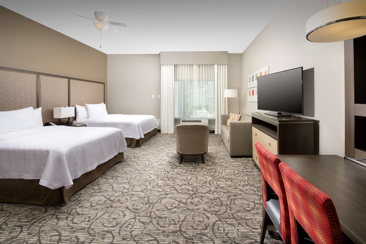 Une chambre d’hôtel avec deux lits, une télévision, un bureau et un petit coin salon.