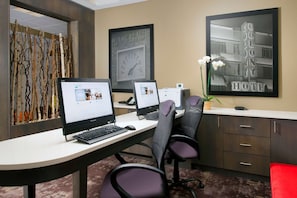 Un espace d’accueil d’hôtel comprenant deux postes de travail informatiques, une horloge et un tableau représentant un bâtiment d’hôtel.