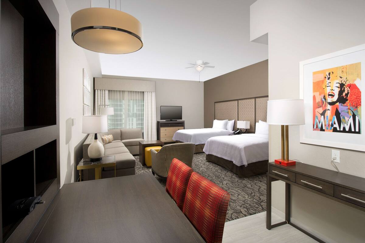 Een hotelkamer met een bed, bureau, televisie, bank en eettafel.