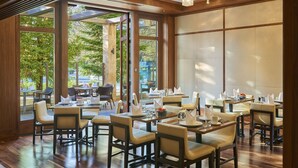 A spacious dining area with multiple tables and chairs, large windows offering views of the outdoors, and a modern interior design with wooden beams and ceiling lights. - Clement Palo Alto – All-Inclusive Urban Resort (Palo Alto)