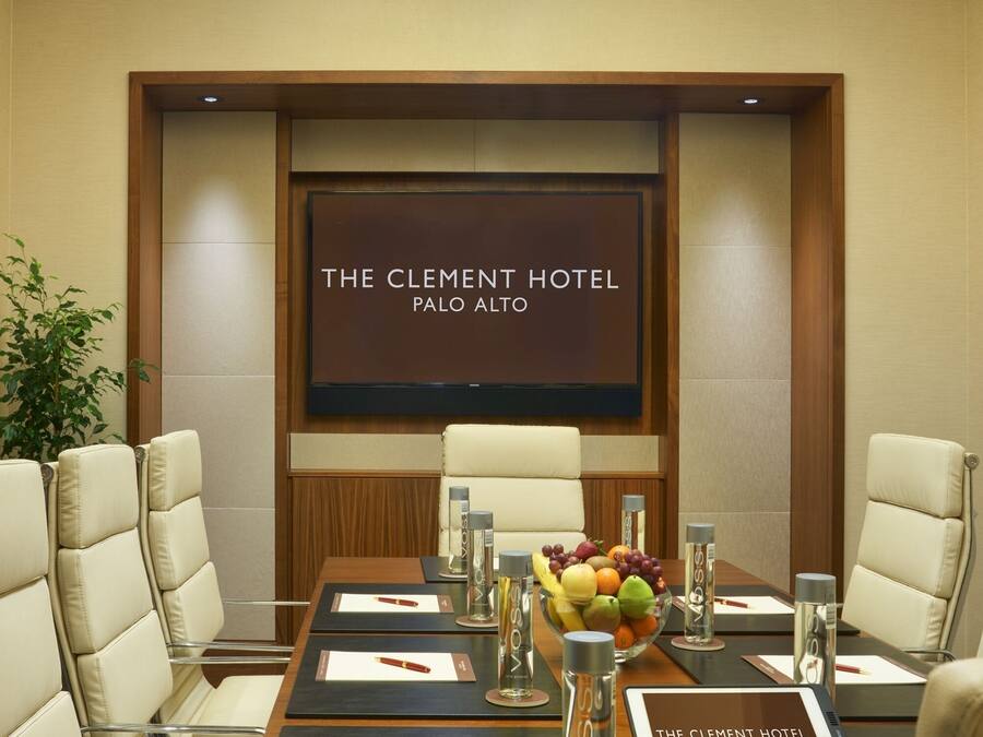 A conference room at The Clement Hotel, Palo Alto, featuring a long table with leather chairs, a fruit bowl, and a digital tablet displaying the hotel name.