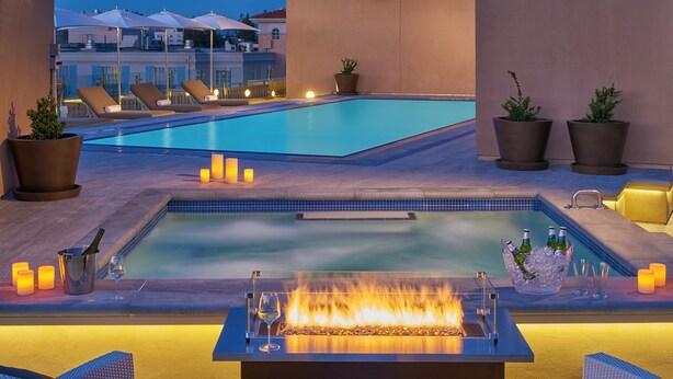 A rooftop pool area with lounge chairs, a fire feature, and potted plants. - Clement Palo Alto – All-Inclusive Urban Resort (Palo Alto)