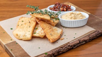 A wooden table with a piece of parchment paper, a white bowl of hummus, and a small bowl of red sauce.