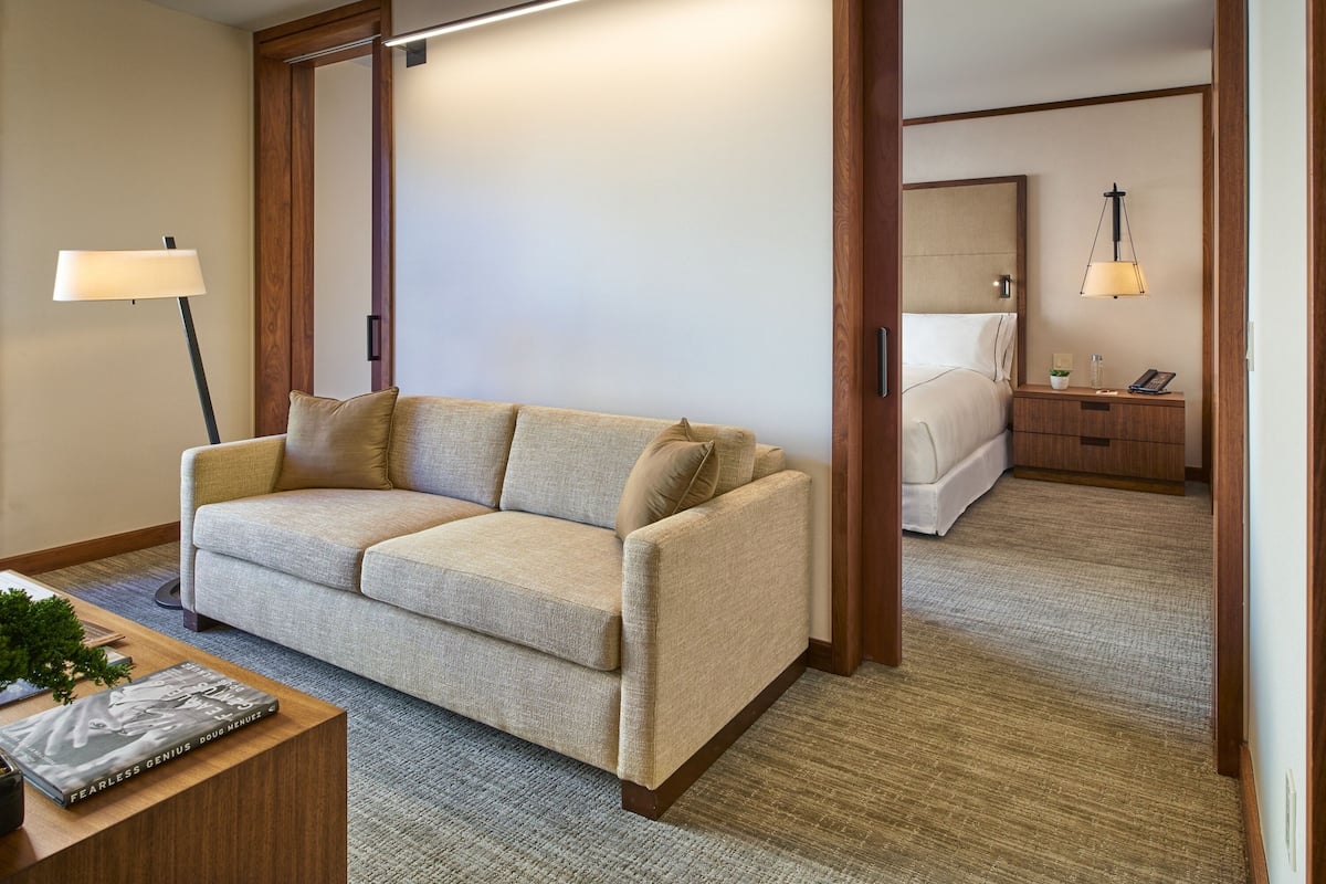 A hotel room with a beige sofa, a wooden coffee table, and a nightstand with a lamp.
