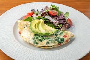 Un plato con una tortilla, rebanadas de aguacate y una ensalada de hojas verdes.