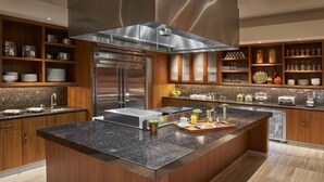 A modern kitchen with a central island, stainless steel appliances, wooden cabinetry, and a variety of kitchenware. - Clement Palo Alto – All-Inclusive Urban Resort (Palo Alto)
