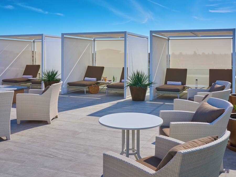 A rooftop terrace with outdoor seating, including wicker chairs and a round table, and a view of the city skyline.