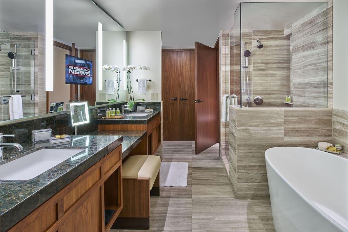 A modern bathroom with a large mirror, a bathtub, a shower area, and a vanity with a sink and countertop.