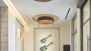 A modern lobby with a wooden reception desk, two guitars on the wall, and a circular chandelier. - Clement Palo Alto – All-Inclusive Urban Resort (Palo Alto)