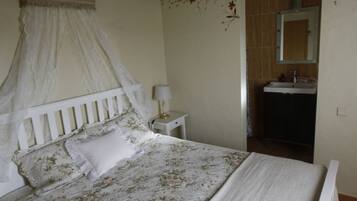 Quarto com cama de dossel, mesa de cabeceira com abajur e banheiro com pia e espelho.