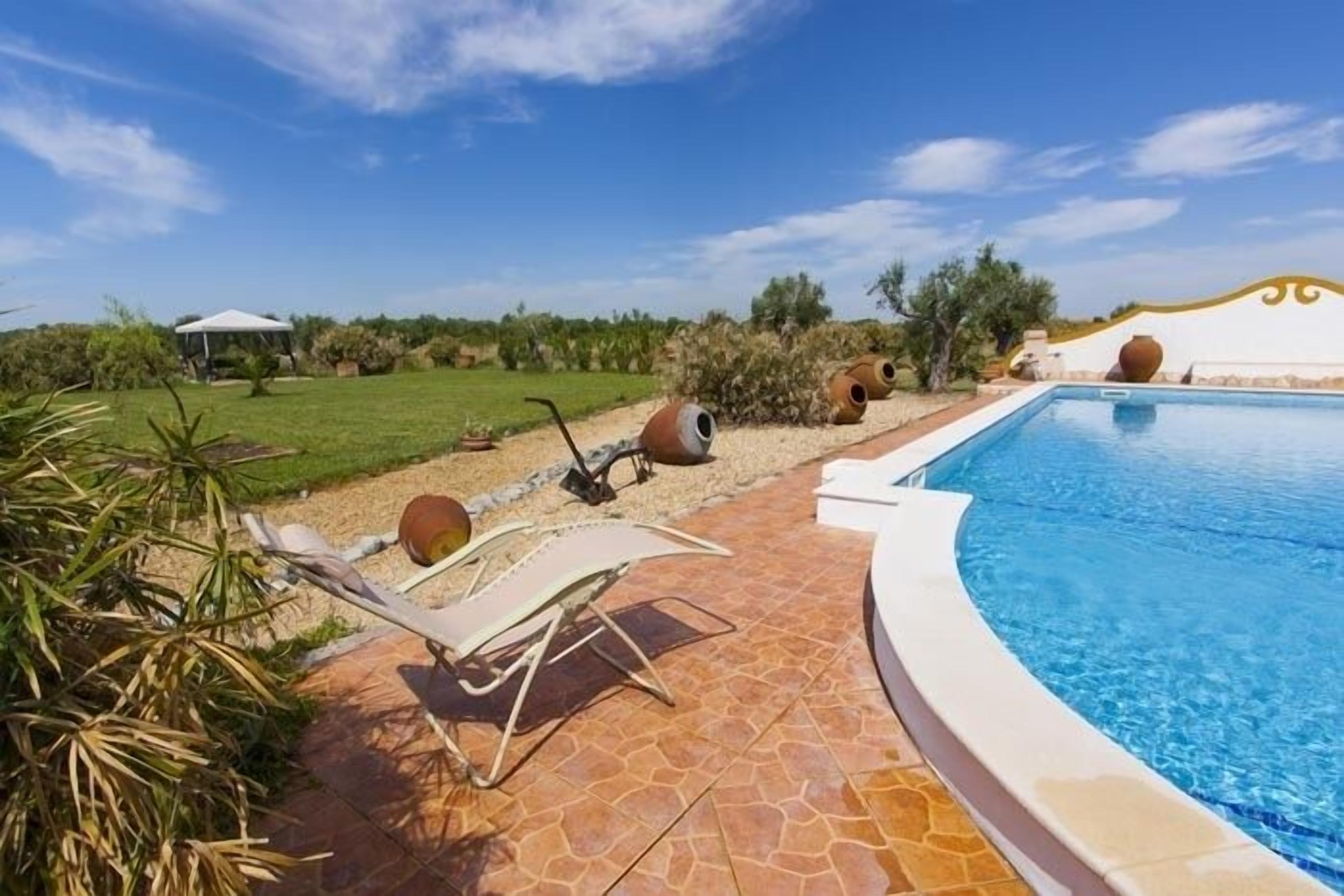 A pool area with lounge chairs, a white umbrella, and a clear blue sky.
