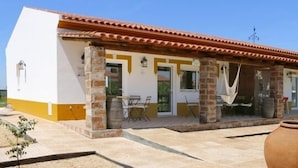 Un edificio de dos pisos con tejado de tejas, pilares de piedra y un patio cubierto con mobiliario exterior.