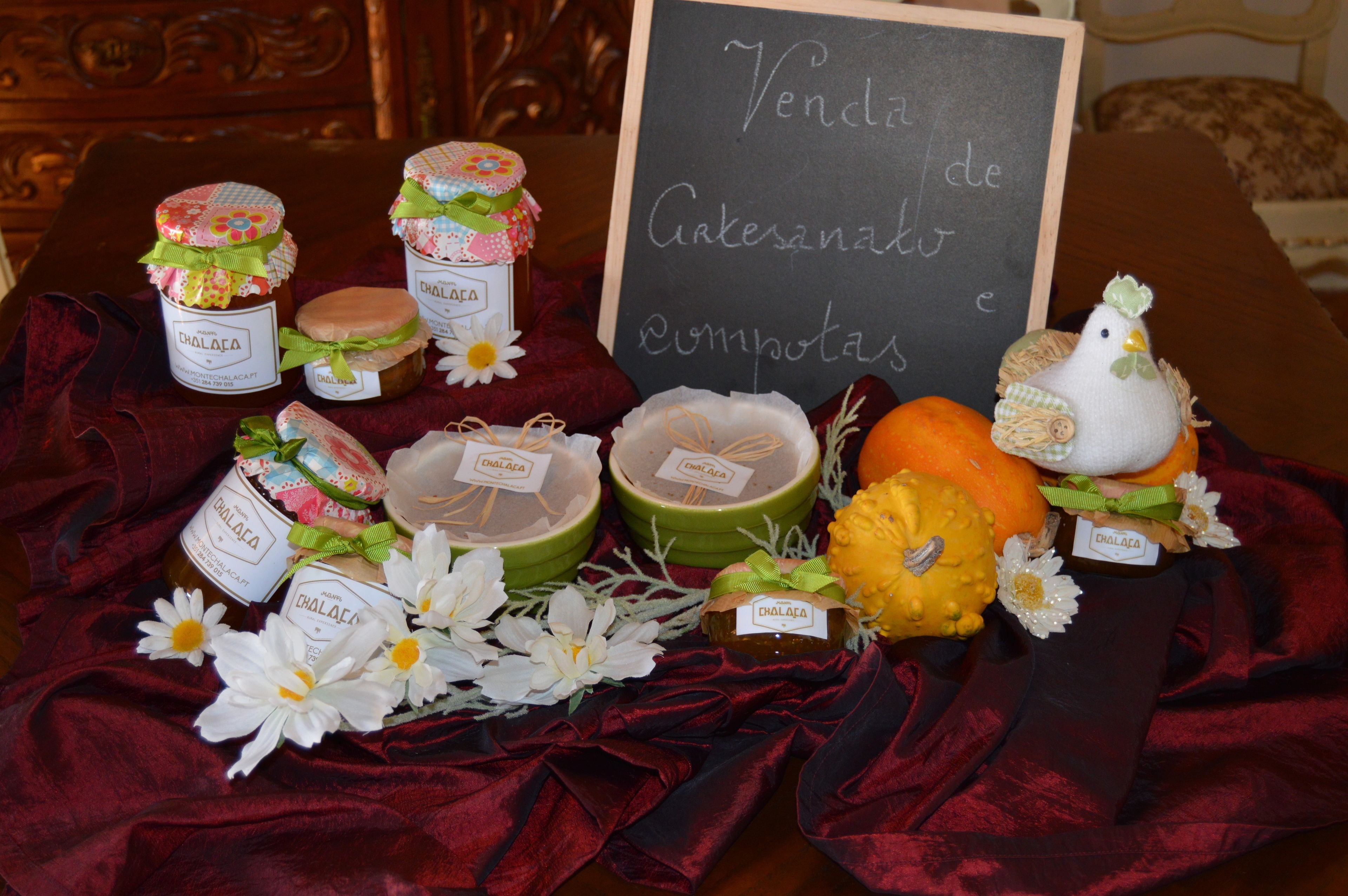 Una exhibición de productos artesanales, incluyendo frascos de miel, un cartel de tiza y objetos decorativos sobre una mesa cubierta con un paño rojo.