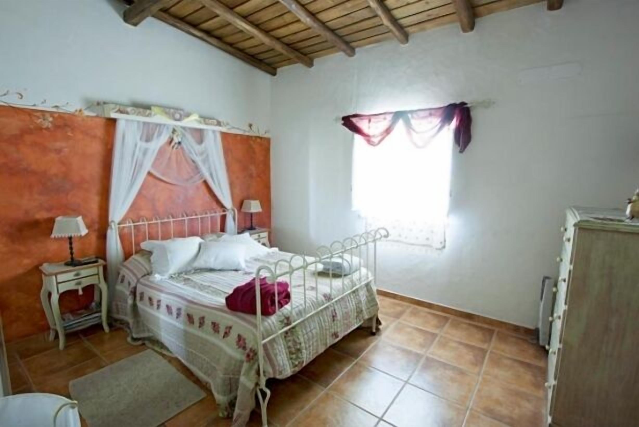 A bedroom with a single bed, a nightstand, a dresser, and a window with curtains.