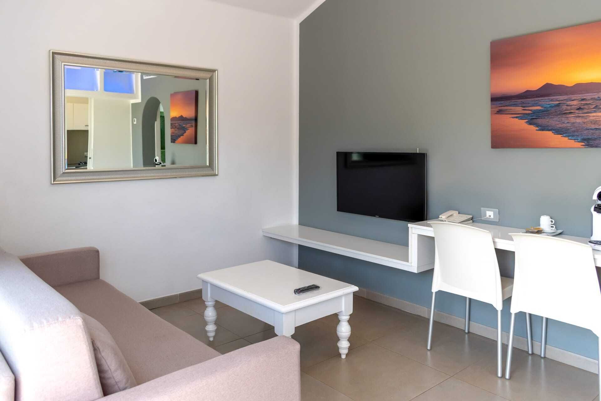 A modern living room with a sofa, a coffee table, a TV mounted on the wall, a desk with a chair, and artwork.