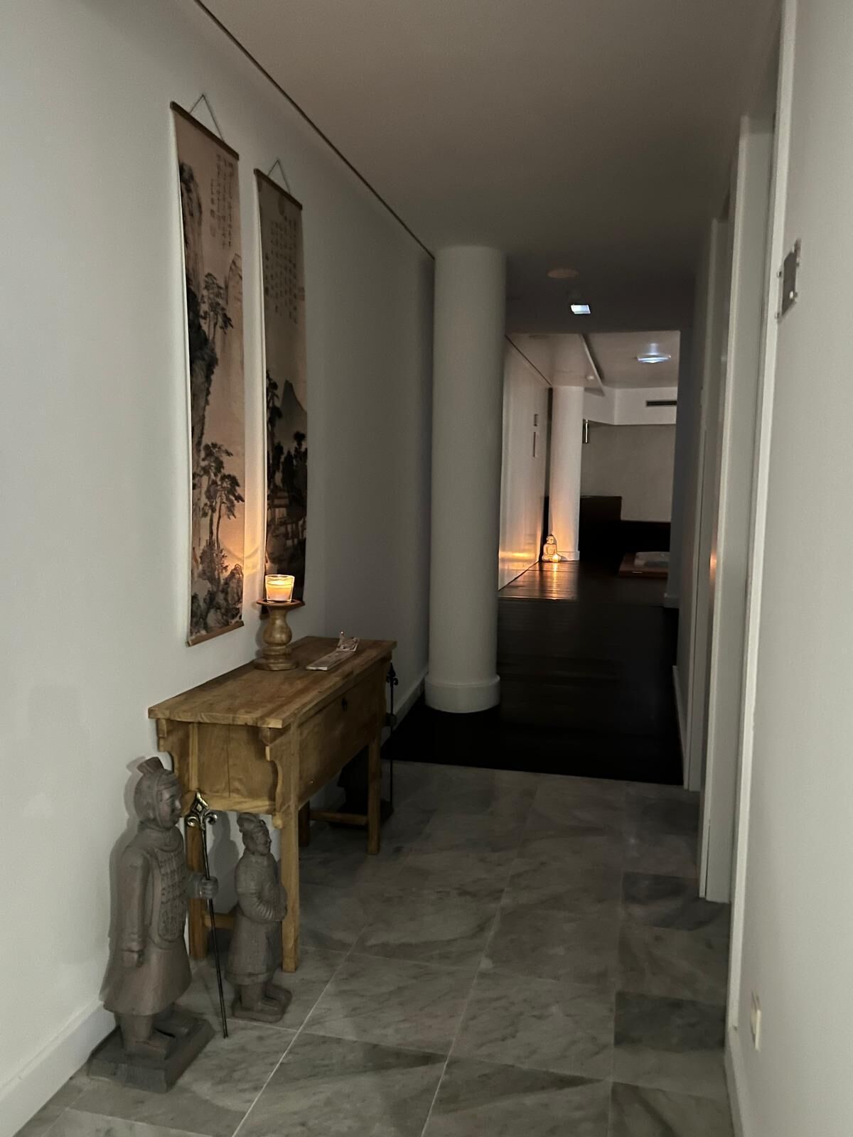A hallway with a wooden console table, a lit candle, and a statue.